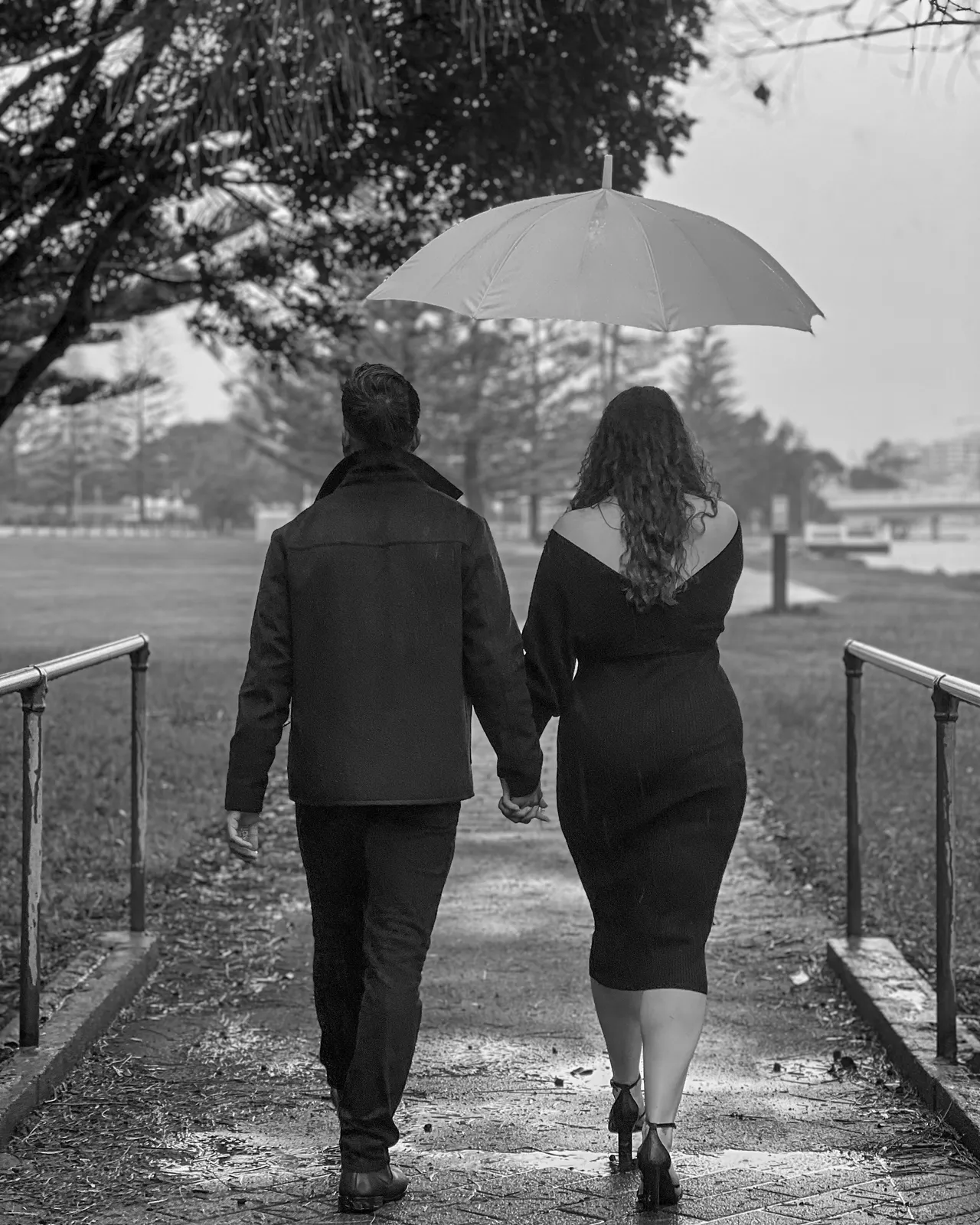 Black and white portrait of a couple walking hand in hand under an umbrella in the rain