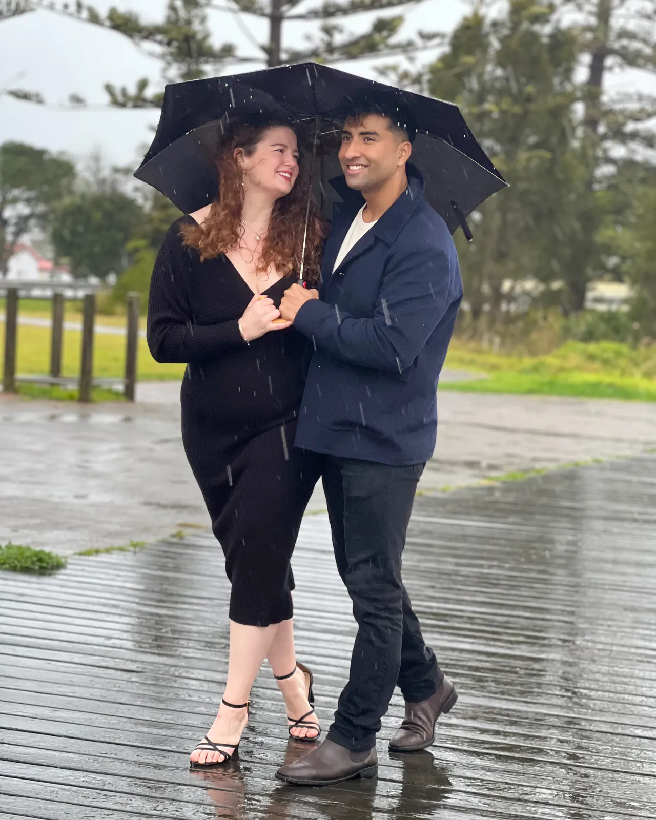 Couple sharing an umbrella and smiling at each other on a rainy boardwalk