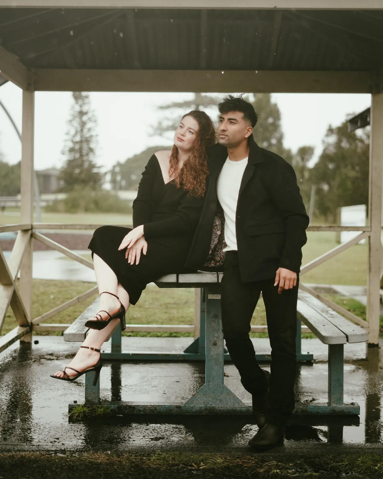 Stylish couple in black posing in a lakeside pavilion for a fashion-inspired portrait session